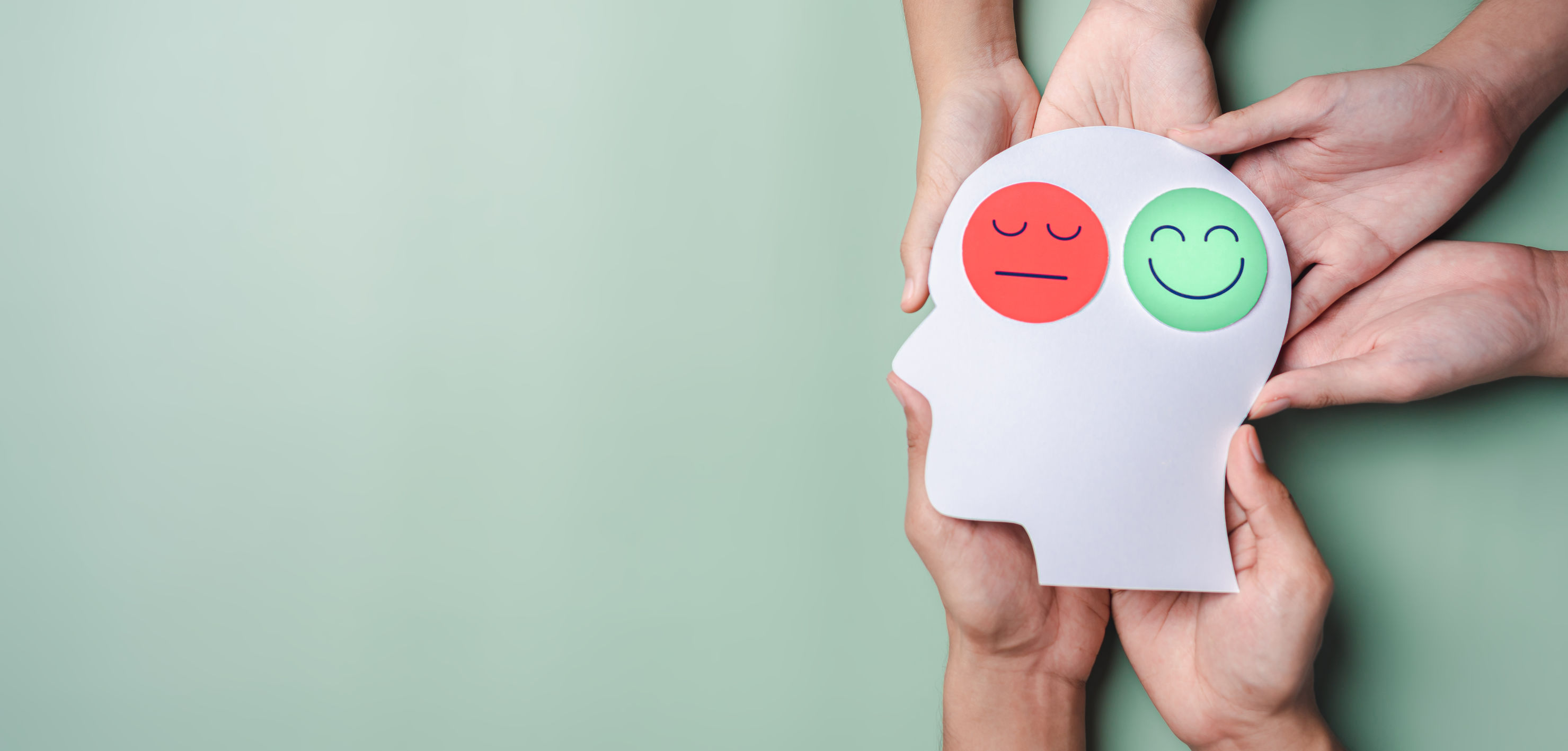 圖像展示多雙手共同托舉白色人頭輪廓剪影，剪影上貼有兩個表情貼紙,分別為左側紅色憂鬱臉及右側綠色微笑臉。